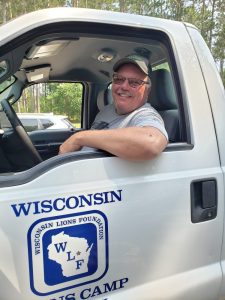 Pete smiling as he sits in his work truck, which is white with a blue Wisconsin Lions Foundation logo on the door. 